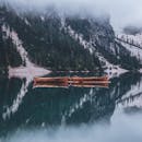 冬日景色静谧，湖面薄雾中泊着小船，倒映着远山与白雪覆盖的森林