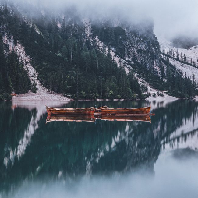 Tranquil winter landscape featuring boats on a foggy lake with mountain reflections and snowy forests.