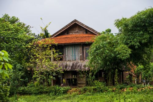 Free Charming rural farmhouse with red tiled roof amidst lush greenery and trees. Stock Photo