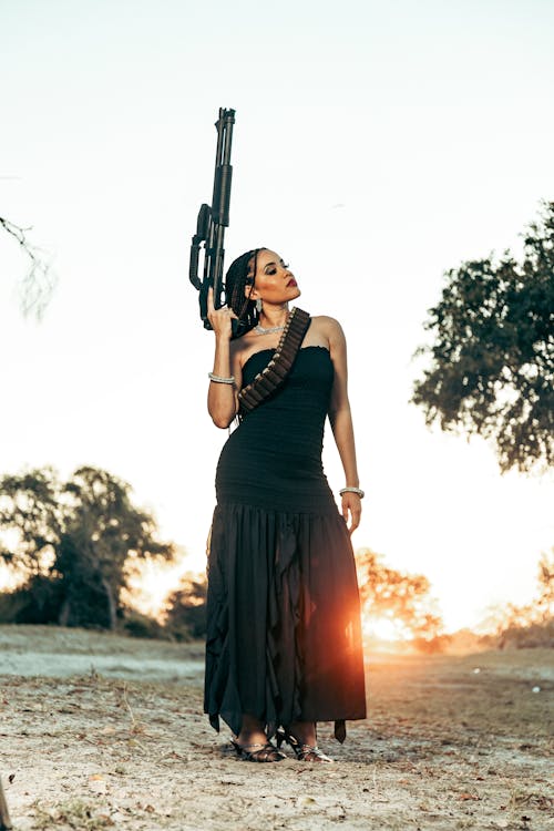 A woman in a black dress holding a gun