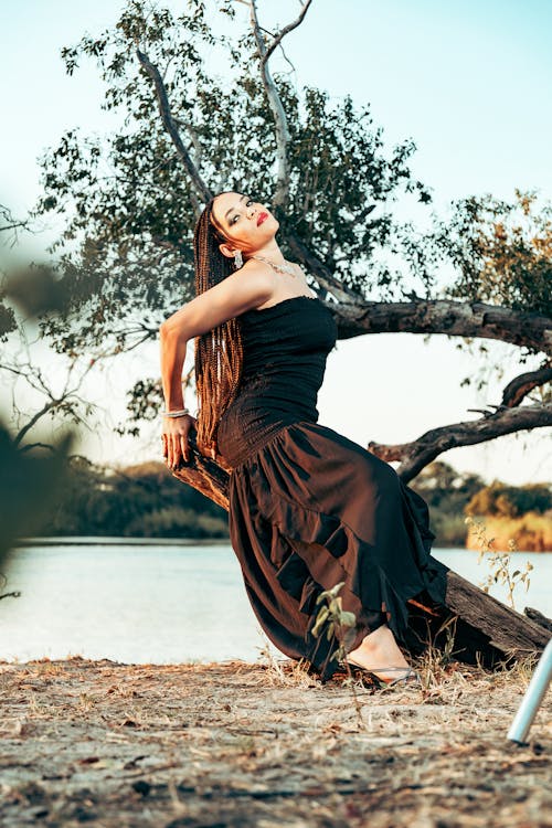 A woman in a black dress posing near a lake