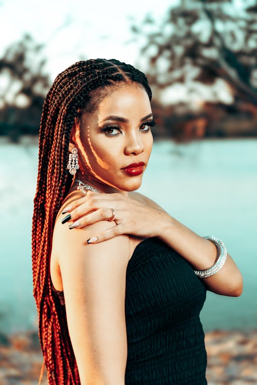 A woman with long braids posing near the water