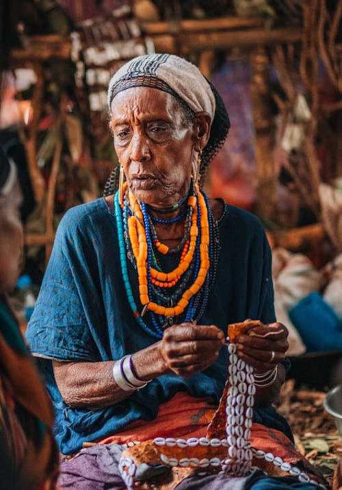 An old woman sitting in a hut with beads on her hands