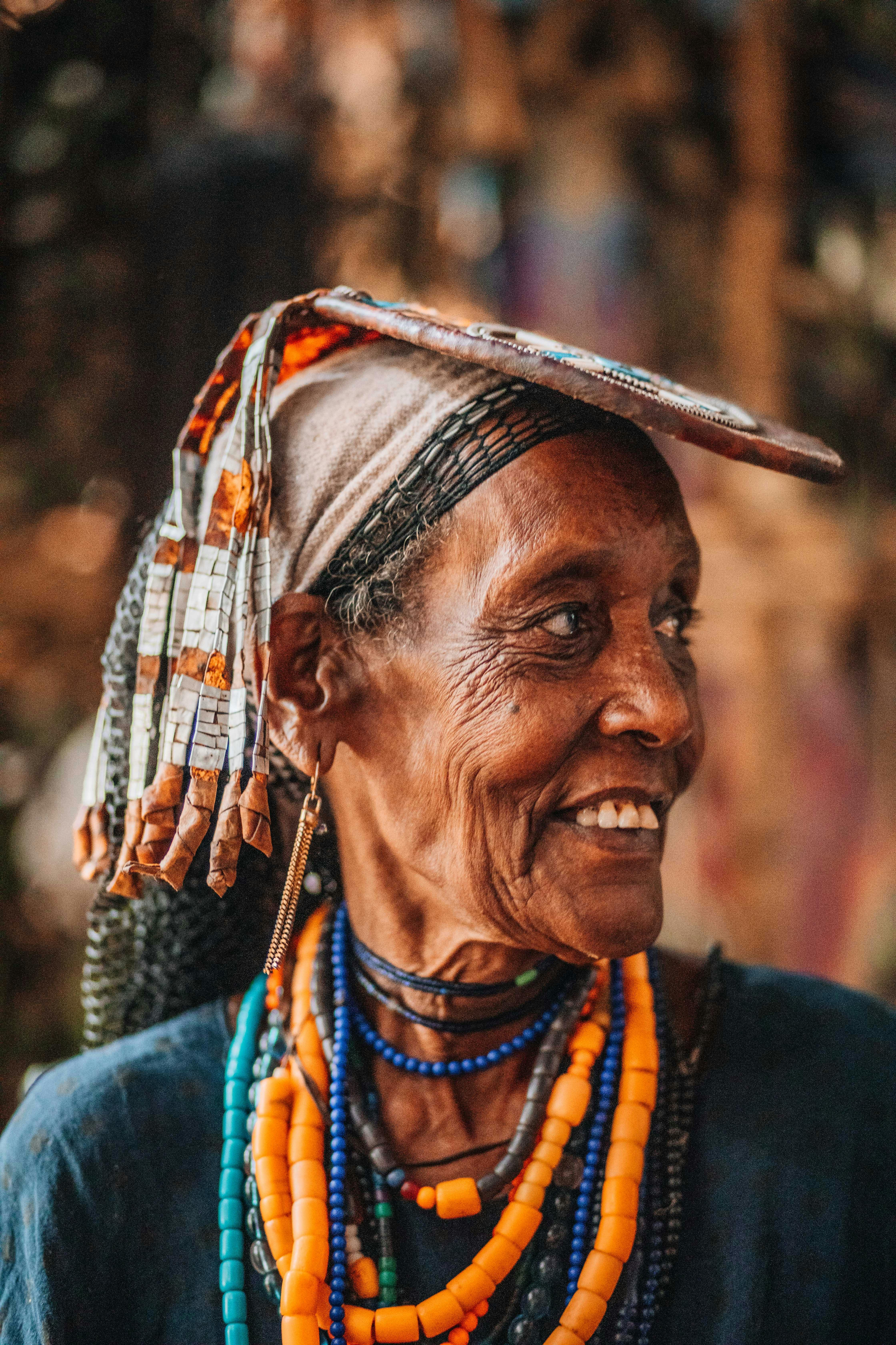 Portrait of an elderly woman wearing traditional beads and headdress, smiling vibrantly.