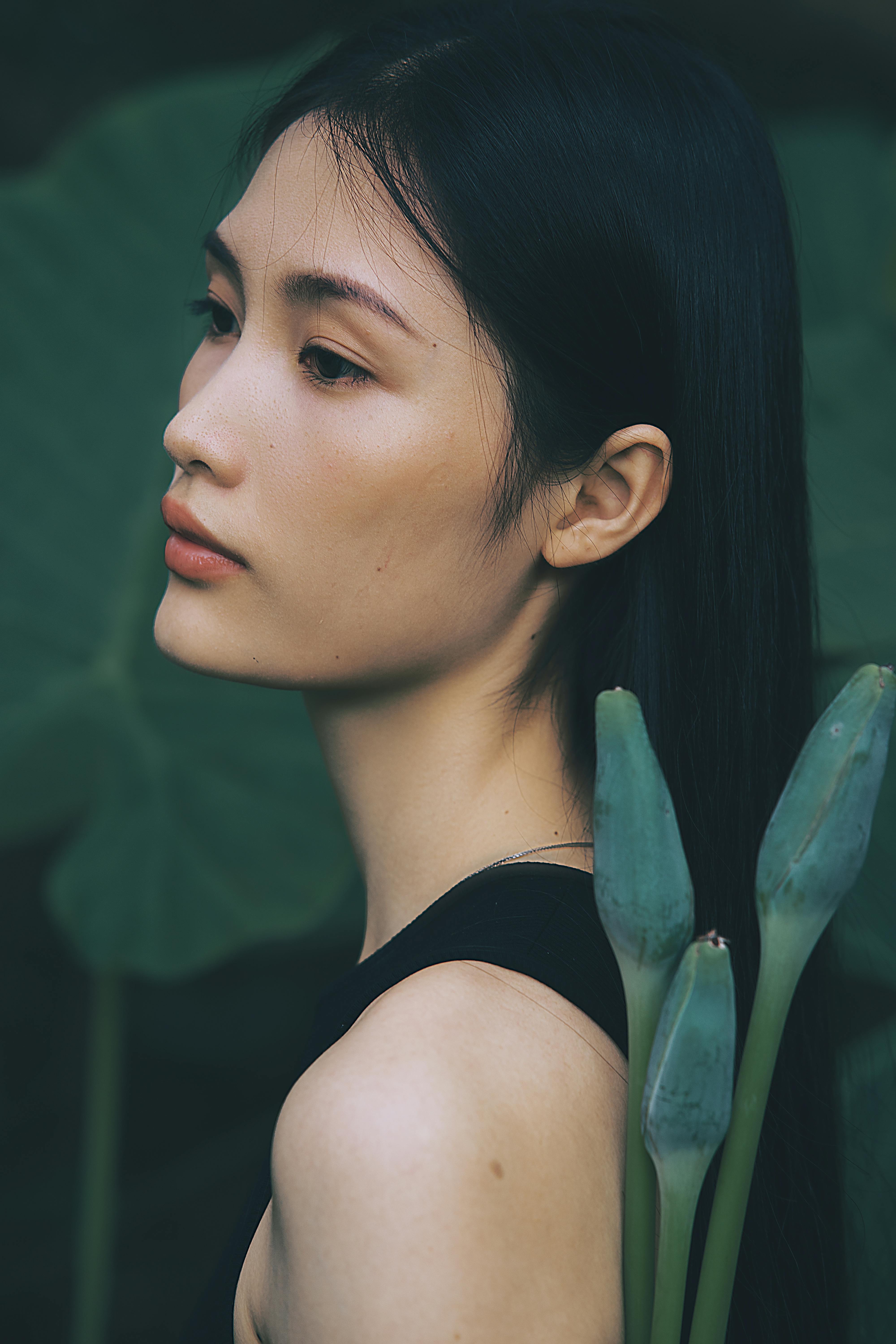 Elegant young woman posing with tropical leaves, exuding a serene and calming presence.