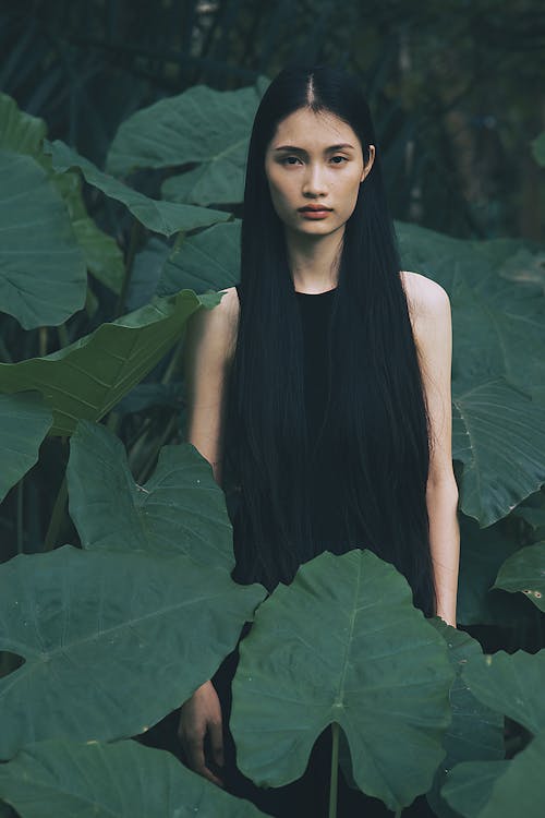 A woman with long black hair standing in front of large leaves
