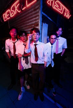 A group of young men in stylish attire under neon lights in a city setting at night.