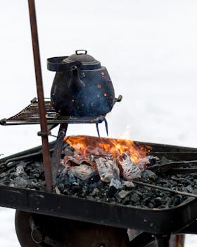 Black kettle heated over an outdoor firepit, surrounded by charcoal. Cozy and rustic scene.