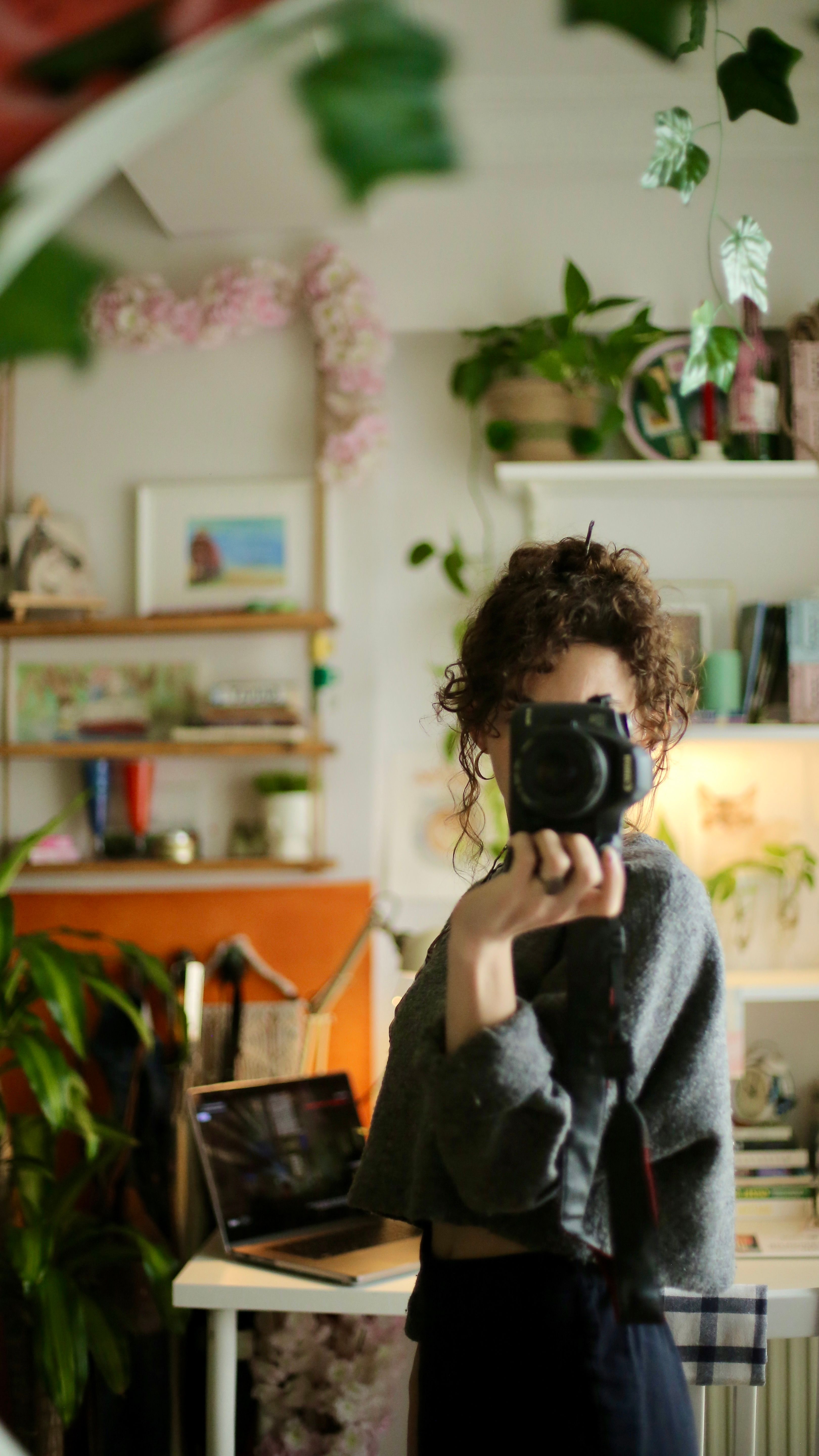 A woman takes a photo of her reflection in a mirror inside a cozy, decorated room.