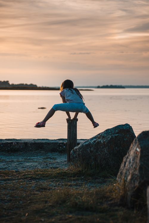 Free A child balances on a post by the waterfront during sunset in Saint-Armel, France. Stock Photo