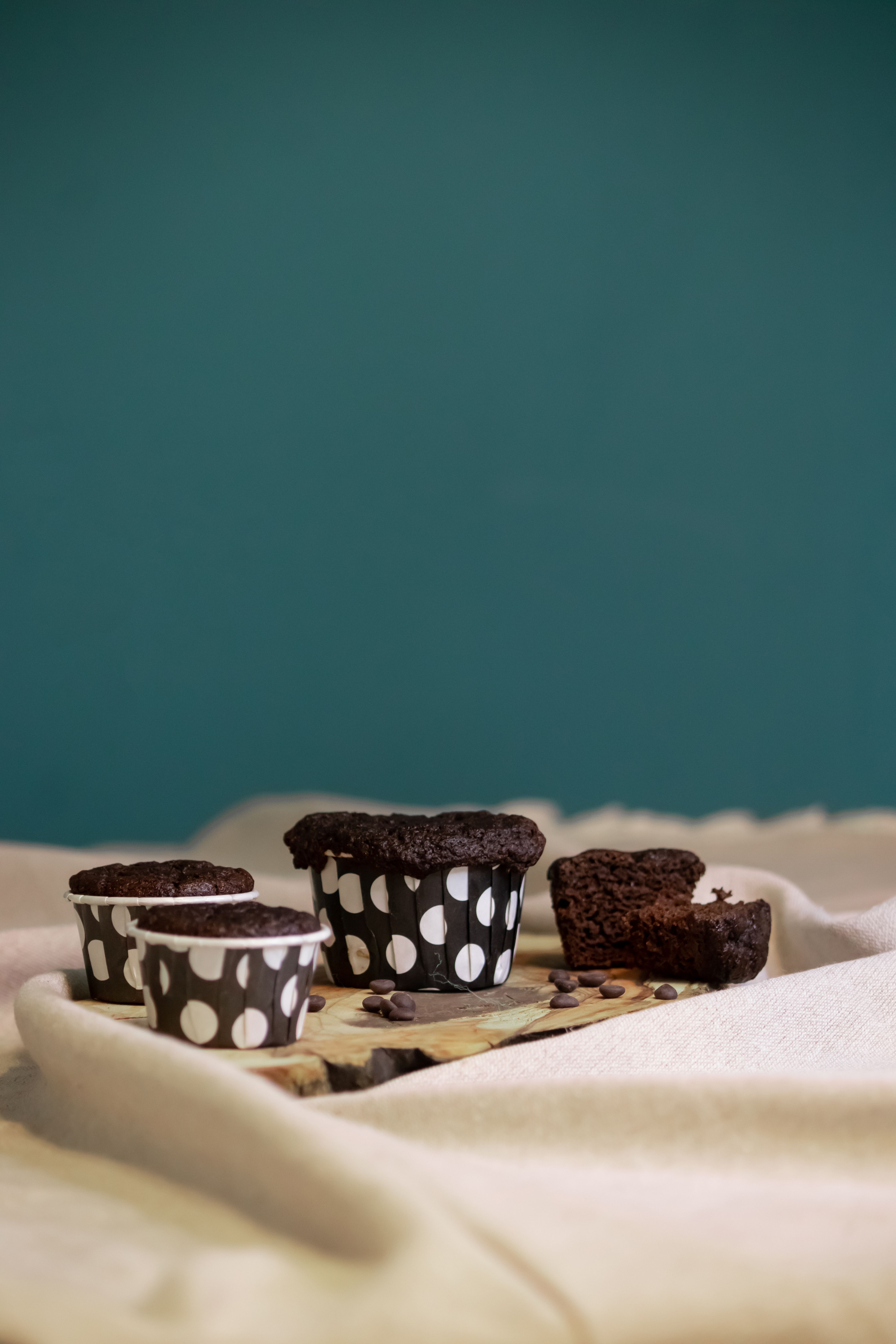 Delicious chocolate brownies in polka dot baking cups on a wooden board with teal background.