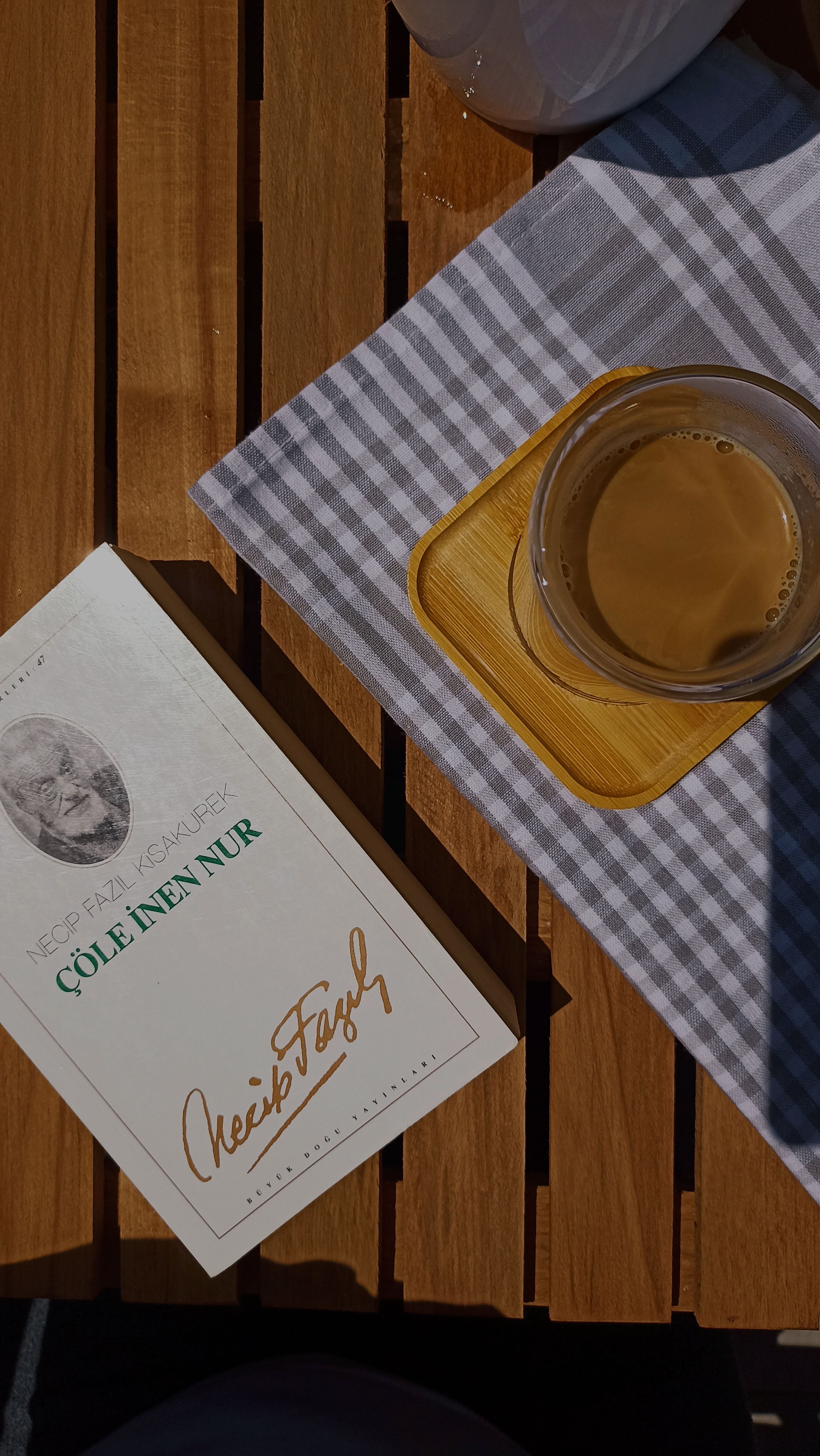 Overhead view of a book and coffee on a wooden picnic table in İzmit, Türkiye.