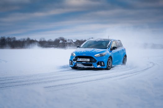 Blue sport compact car drifting on a snowy road in a rural winter setting.