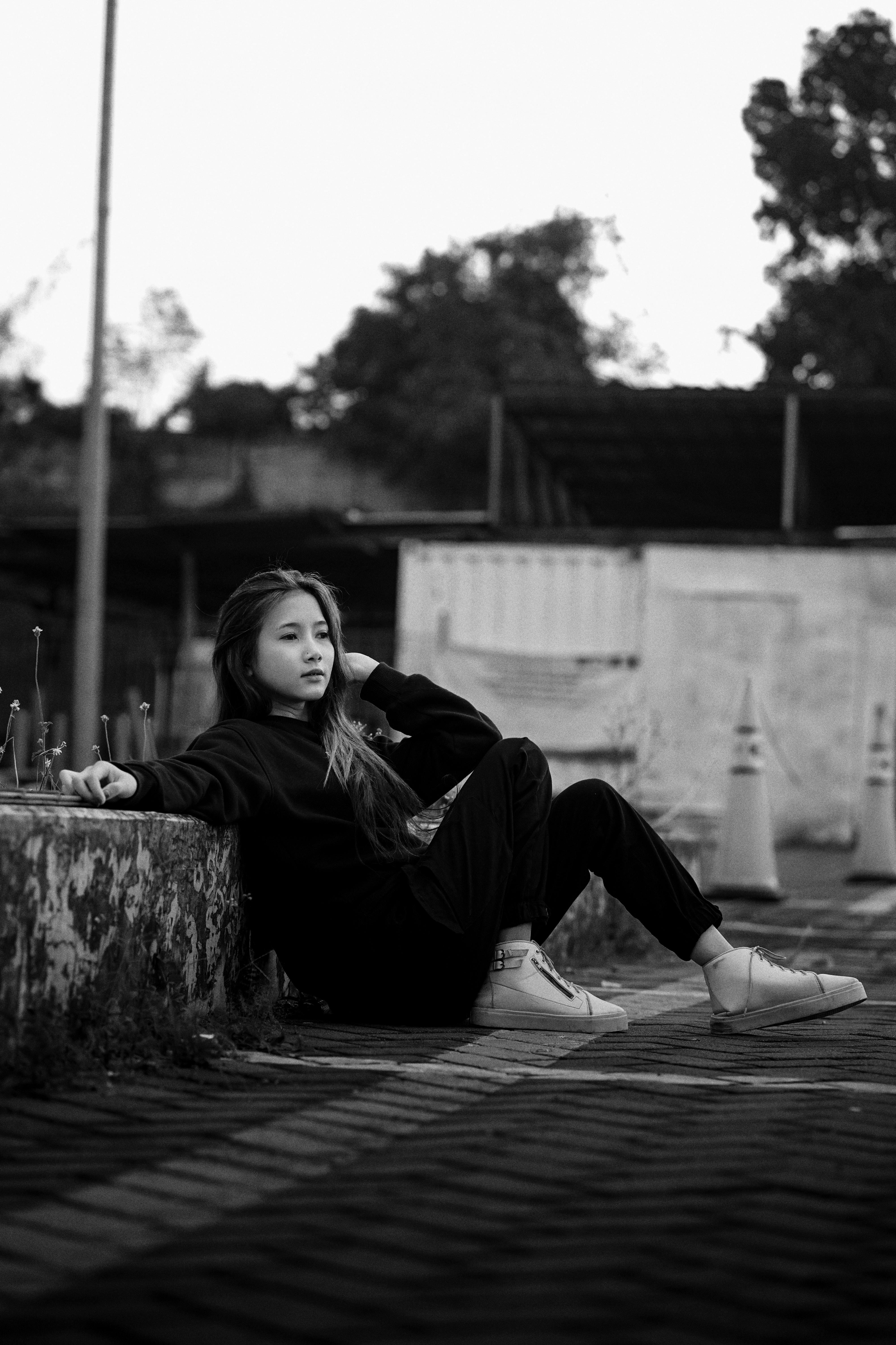 Black and white portrait of a young woman in urban setting, displaying relaxed fashion style.