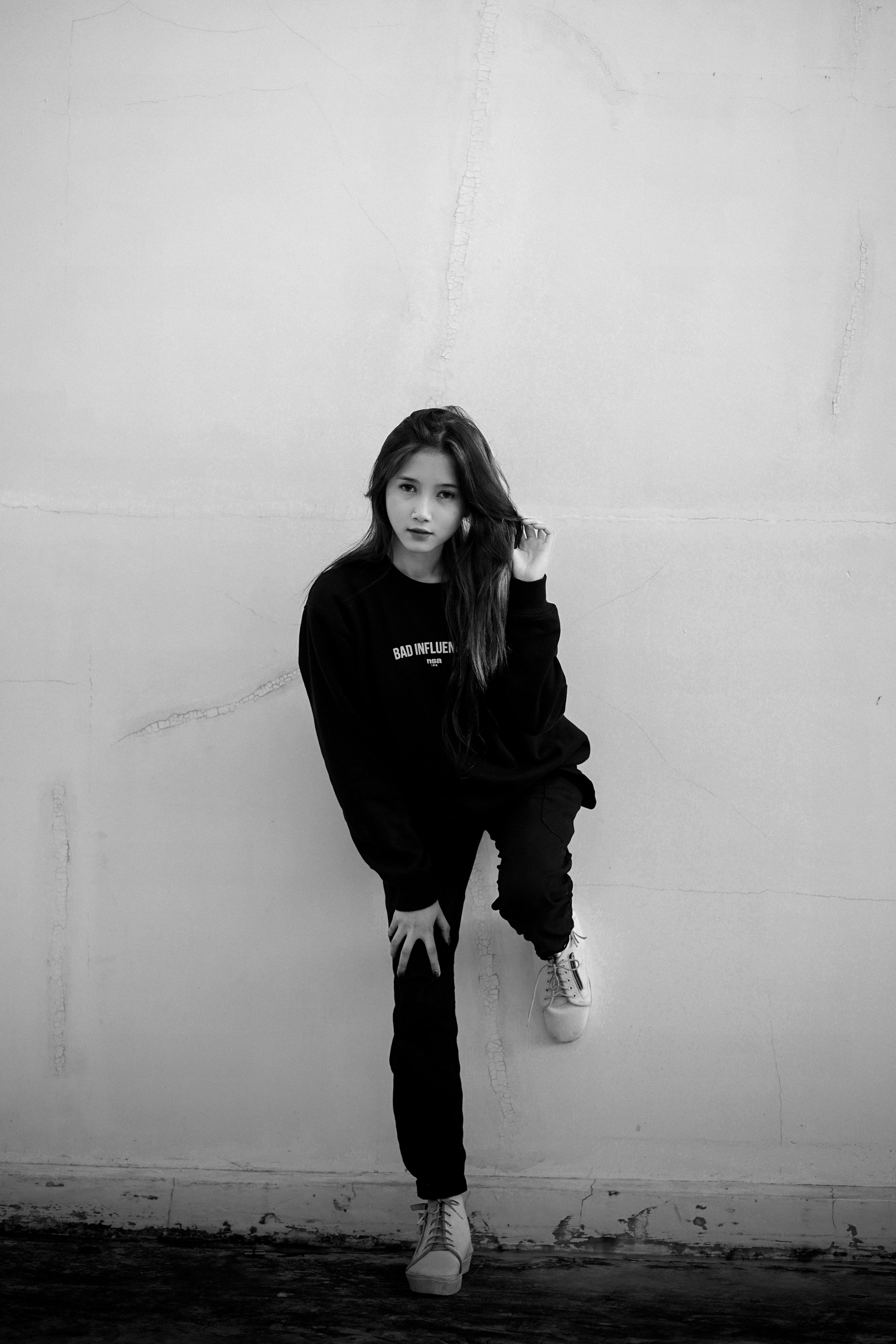 Fashionable woman with long hair posing against an urban wall in a black and white style.