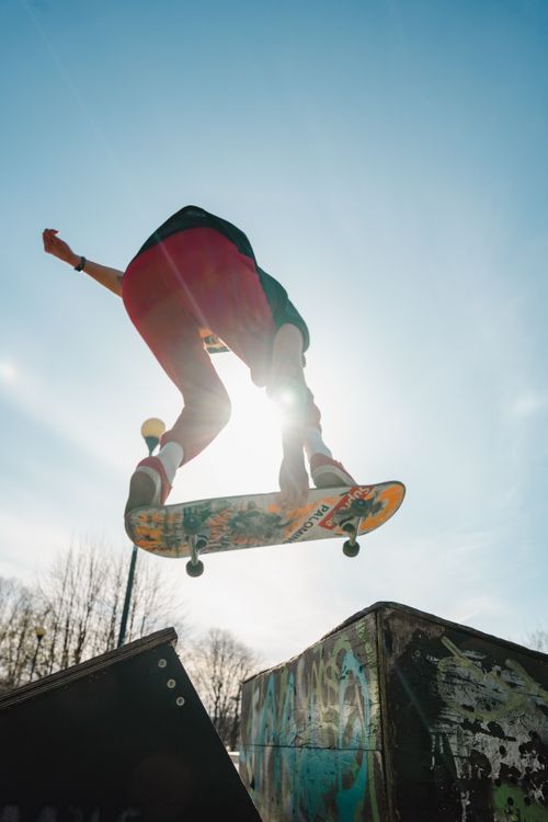 Free Skateboarder performing an aerial trick at a skatepark during sunset. Vibrant urban scene. Stock Photo