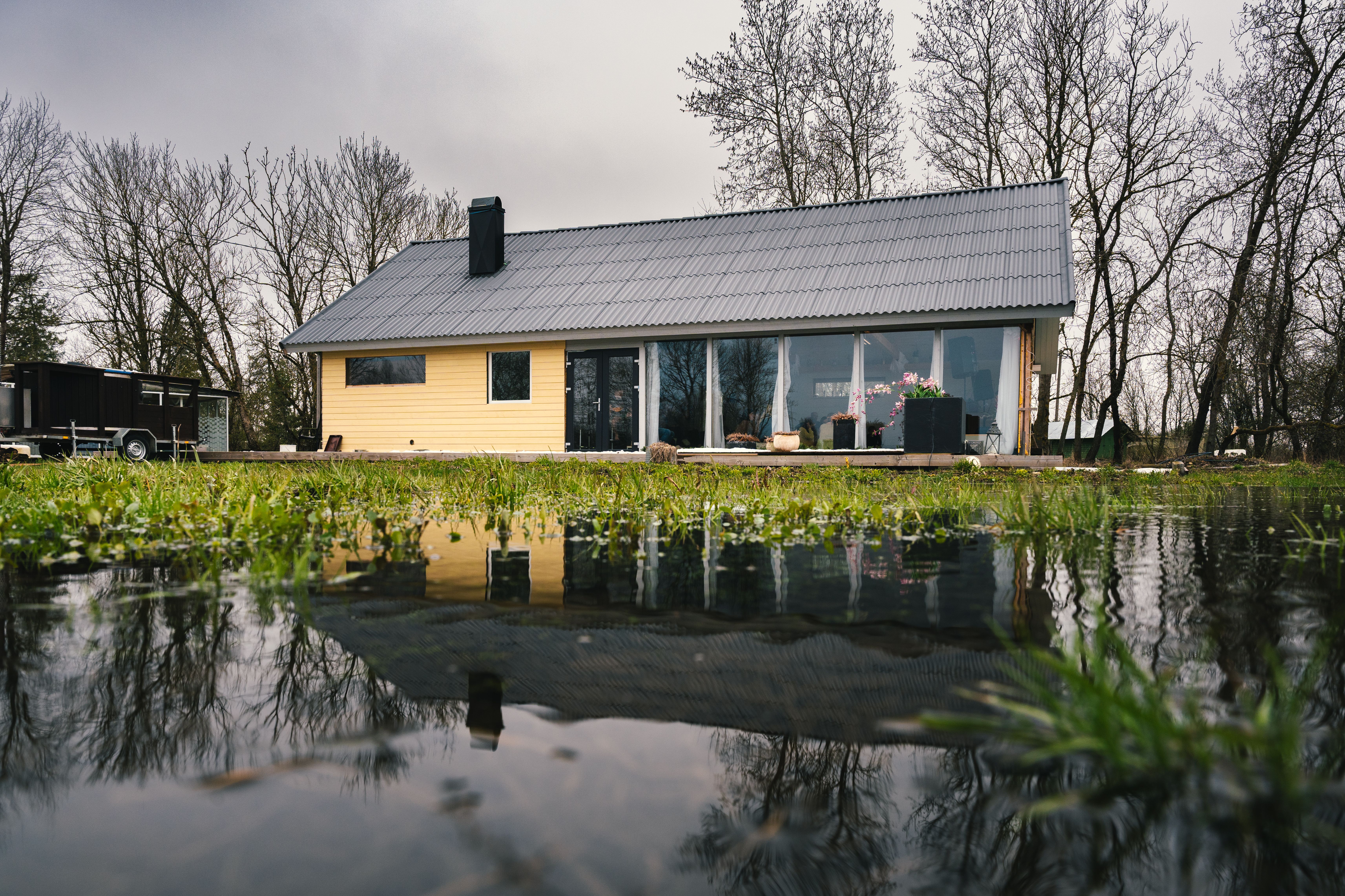 A picturesque rural house next to a reflecting pond surrounded by budding trees.