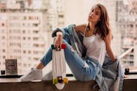 在城市环境中，一位穿着休闲装的时尚女性在窗前拿着滑板