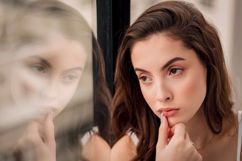 Free A pensive woman looks out a window, her reflection creating a thoughtful portrait. Stock Photo