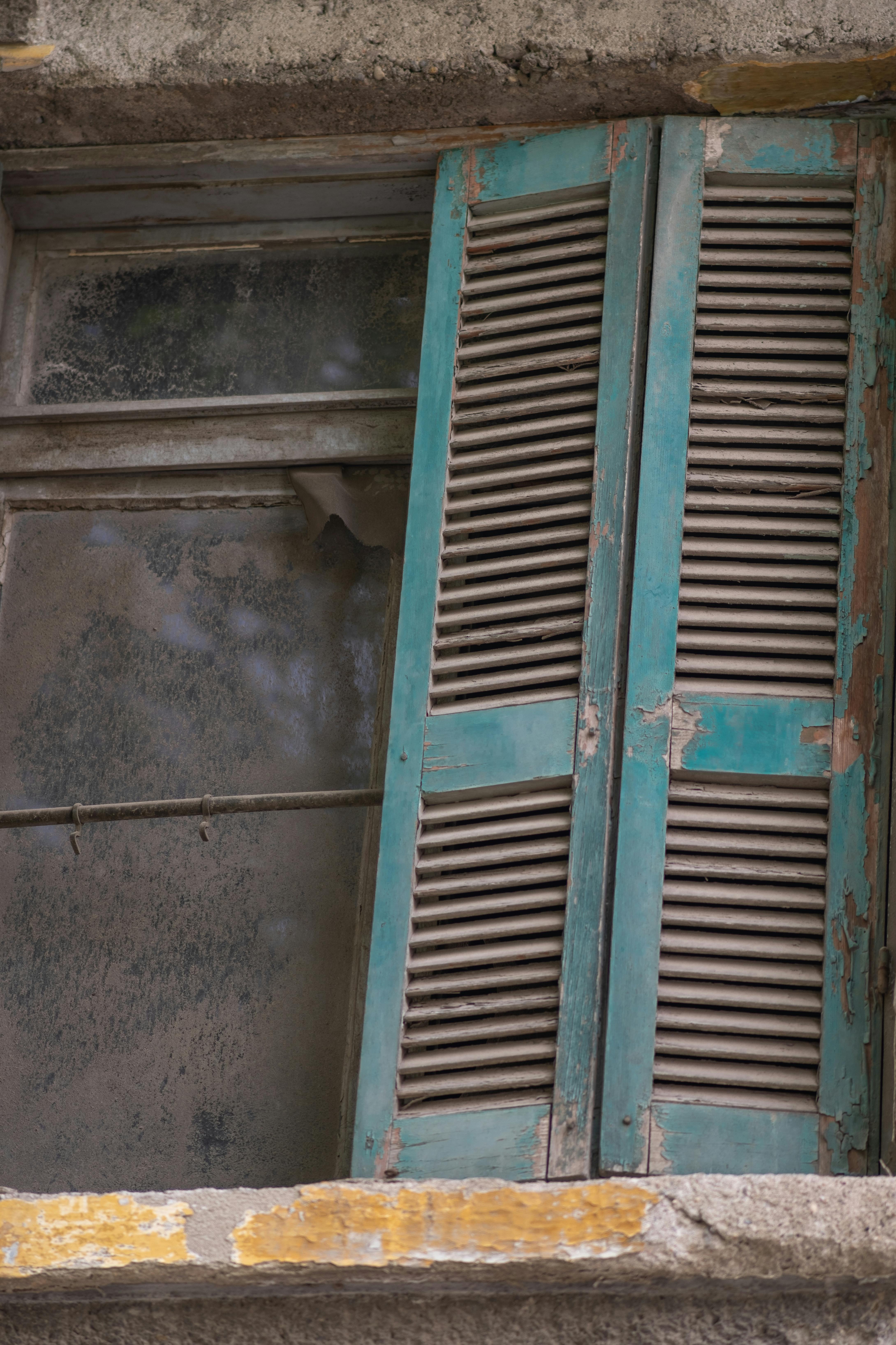 A textured, weathered window with rustic blue shutters in Izmir, Türkiye.
