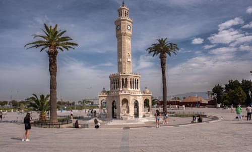 A clock tower in a plaza with palm trees