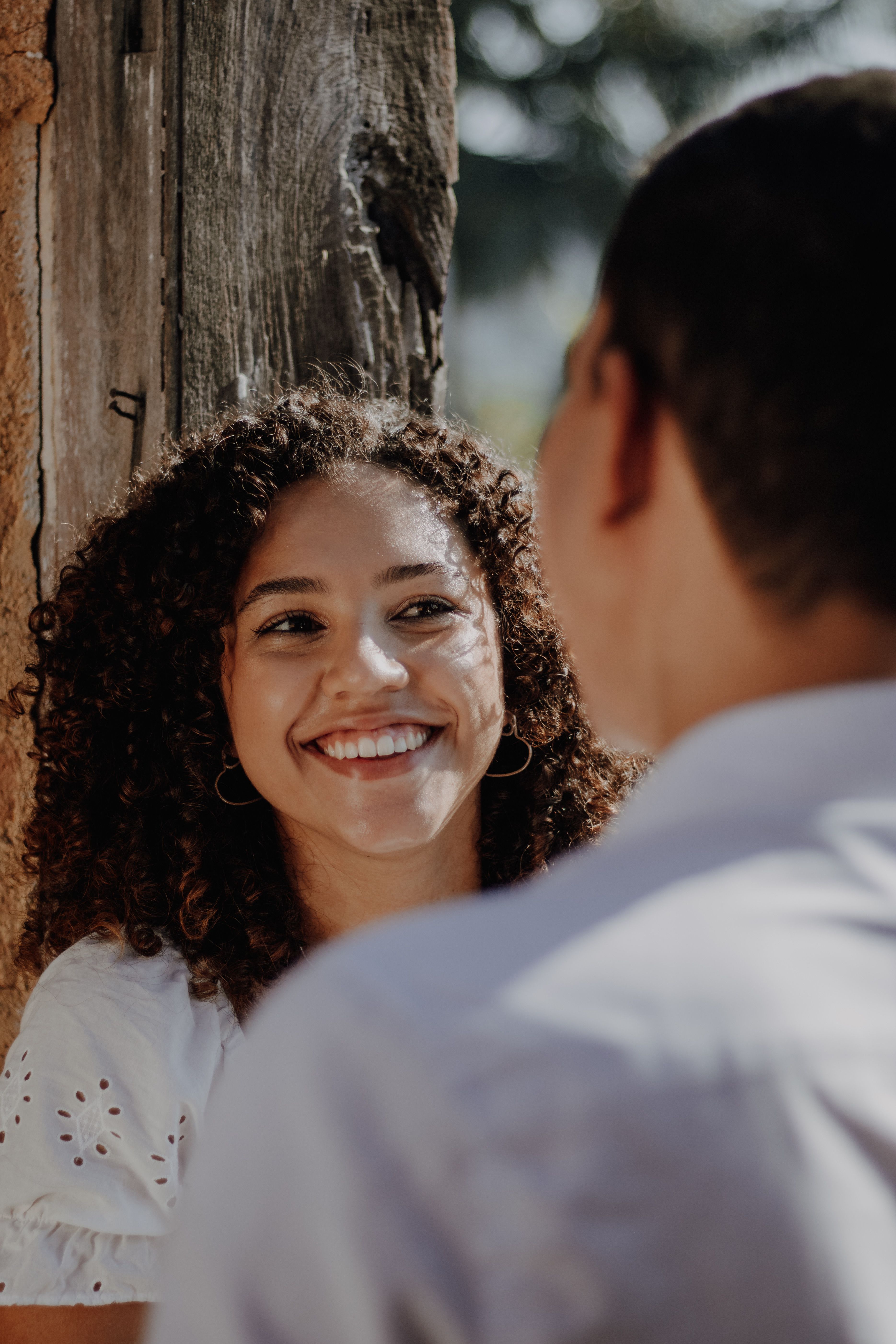 A couple enjoys a light-hearted moment outdoors, focusing on a smiling woman with curly hair.