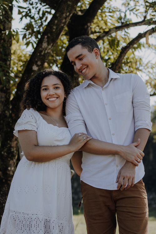 Free Smiling couple in white outfits enjoying a beautiful day outdoors under a large tree. Stock Photo