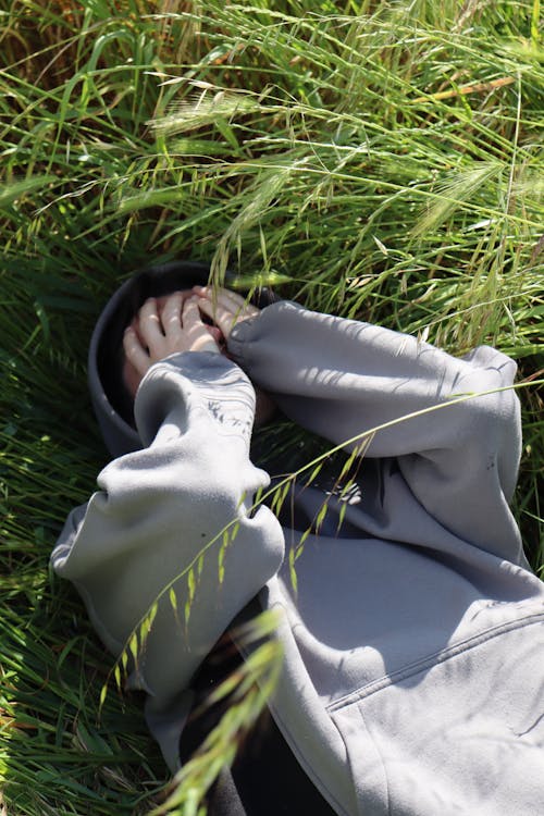 Free Person in Gray Hoodie Lying Down with Face in Hands on Grass Stock Photo