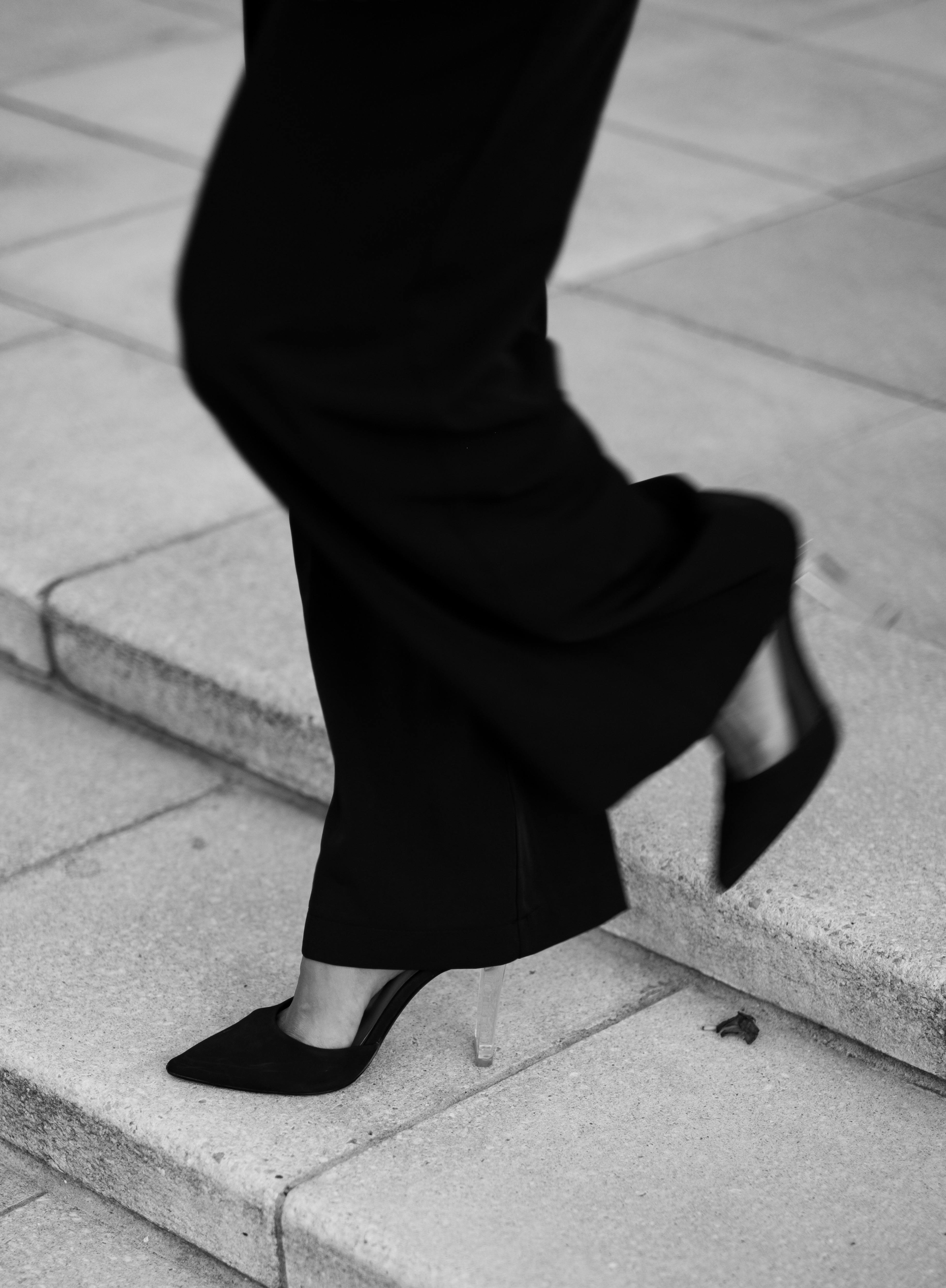 Black and white photo of a woman in heels walking up steps, showcasing urban elegance.