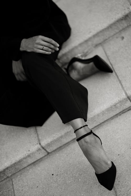 A woman in black shoes and a black dress sitting on steps