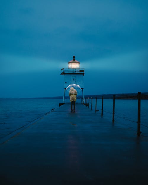 Photo of a Person Standing on Footbridge Leading to a Lighthouse