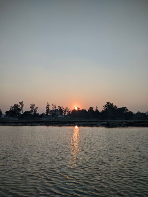 Free Peaceful sunset over a calm lake with a tree-lined horizon, capturing nature's beauty. Stock Photo