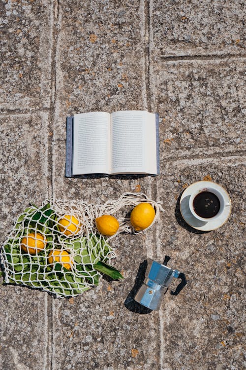 Free Book, Coffee, Coffee Pot and Torn Bag of Lemons on Pavement Stock Photo