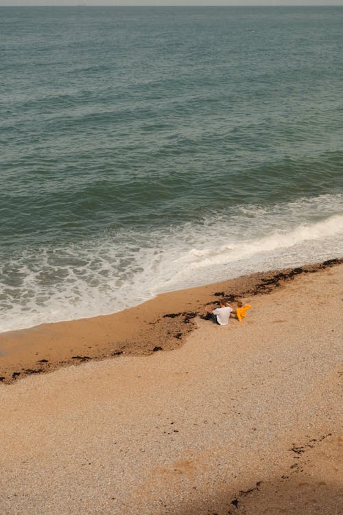 A person is sitting on the beach with a surfboard