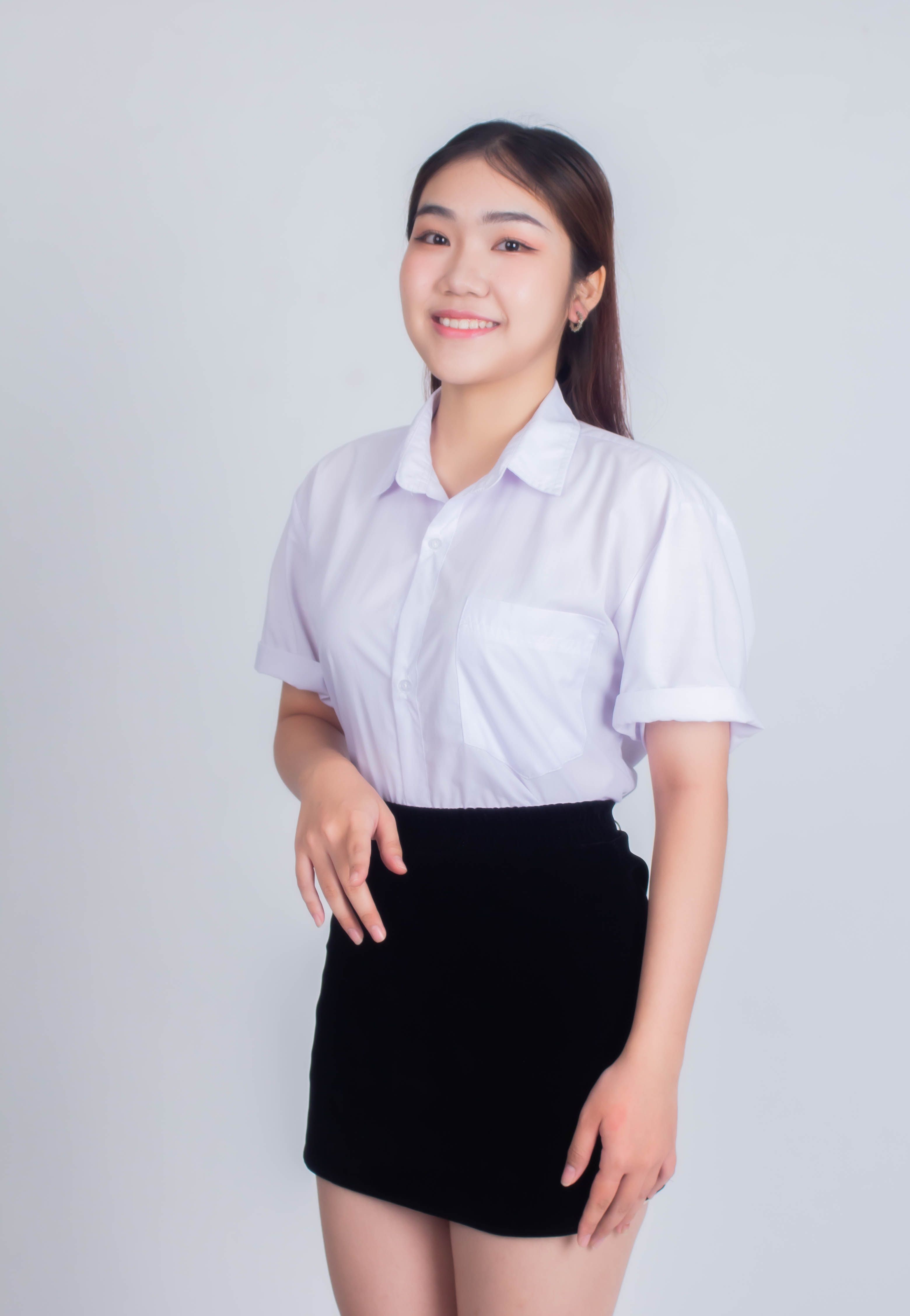 Cheerful young woman standing against a white backdrop, showcasing modern office attire.