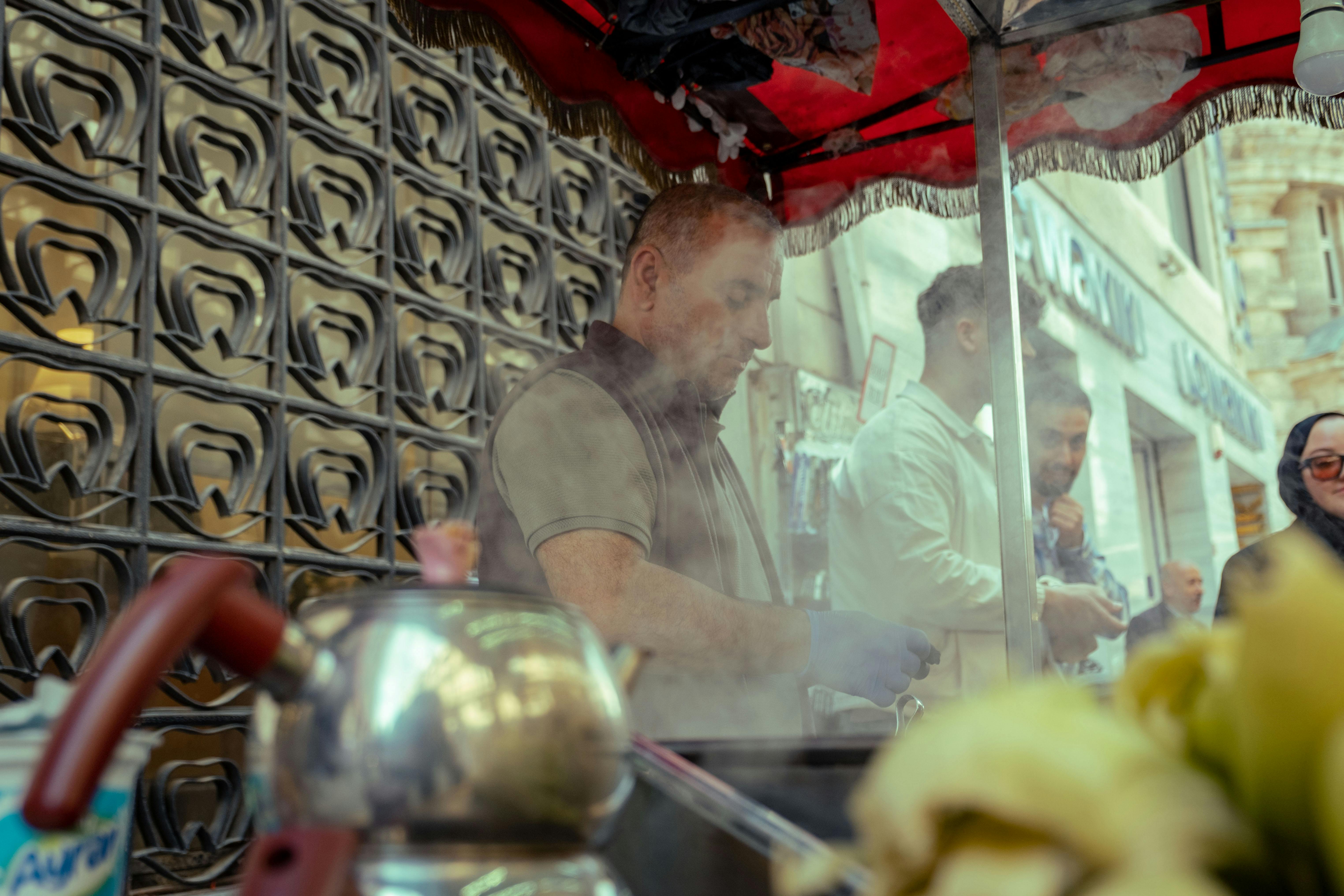 Street vendor cooking delicious food at a bustling market with smoke rising in an urban setting.