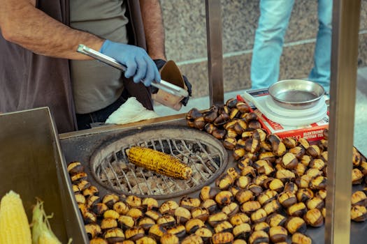 A vendor roasting chestnuts and corn on an open grill at a street food stand.