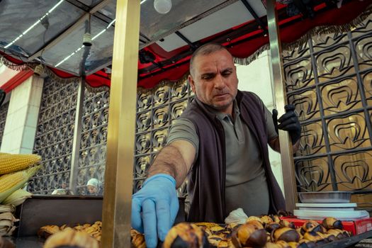A street vendor roasts and sells fresh chestnuts at an outdoor market stand during the day.