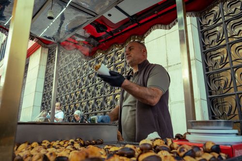 Free Man selling roasted chestnuts at a busy urban food stand, adding local flavor to the city scene. Stock Photo