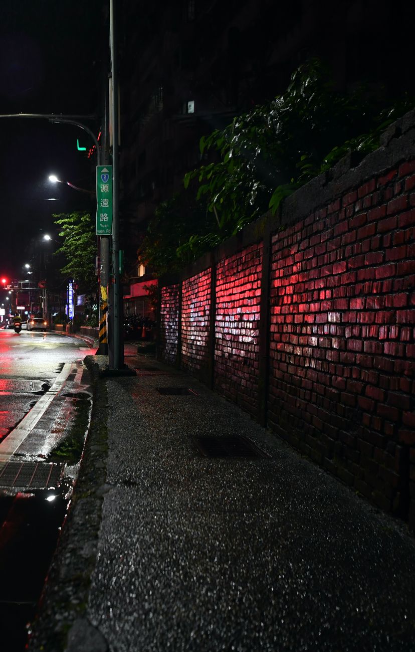 Capture of a rainy urban street at night with reflections and a wet sidewalk.