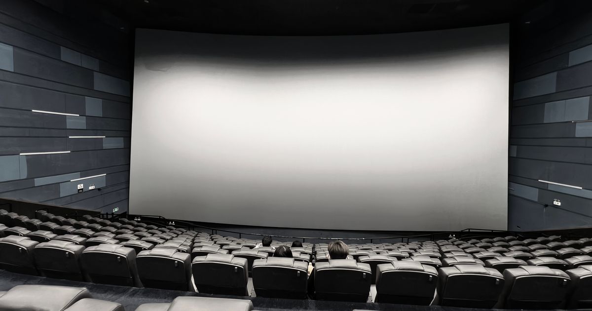 Spacious empty movie theater with a few people seated and a large blank screen.