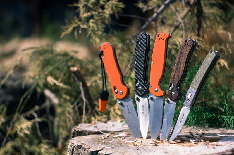 A collection of stylish pocket knives displayed outdoors on a tree stump.