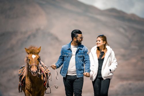 Free A couple holding hands while walking with a horse in a beautiful mountain landscape. Stock Photo