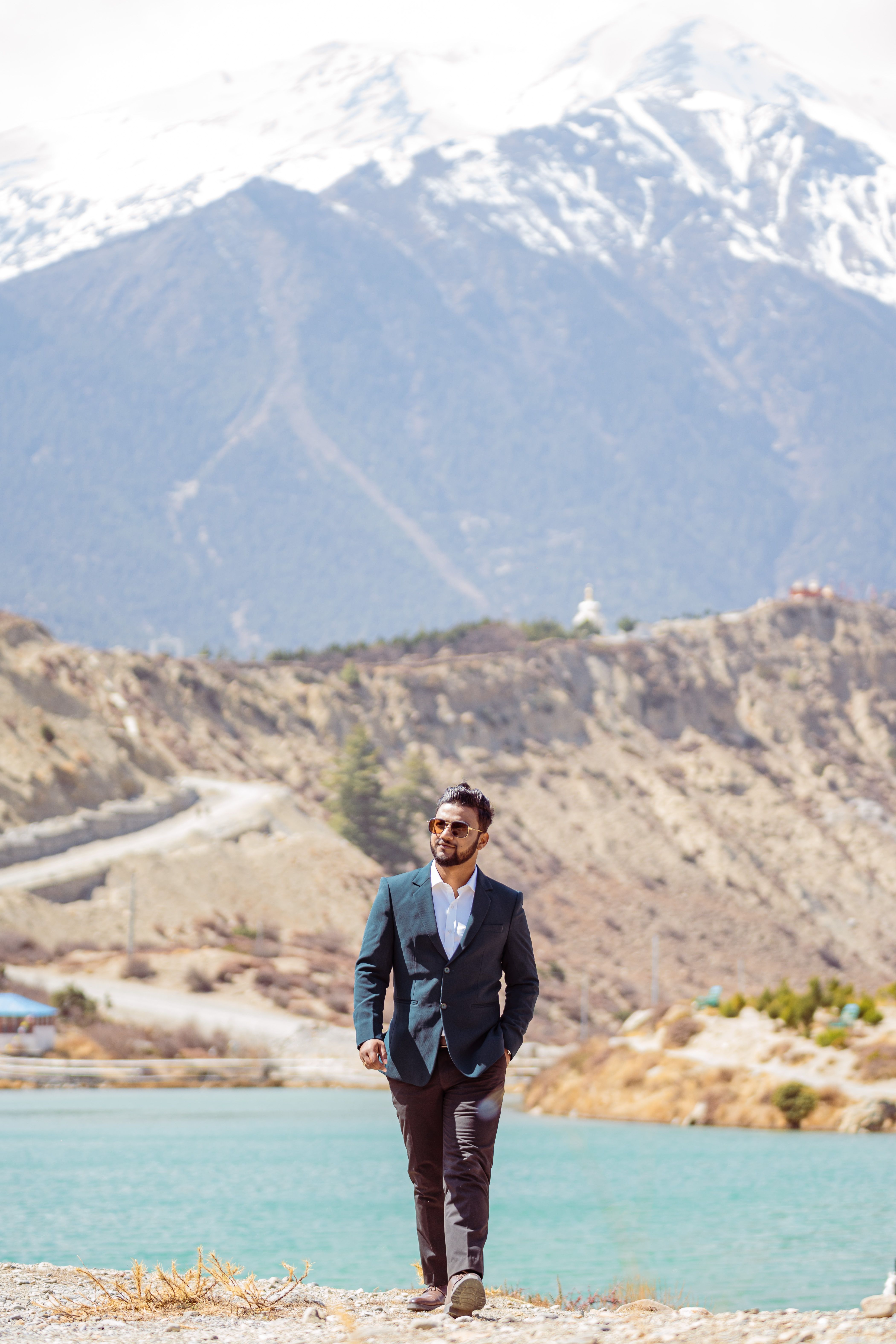 Stylish man in a suit walking by a lake with stunning mountains in the background. Perfect for travel and fashion themes.