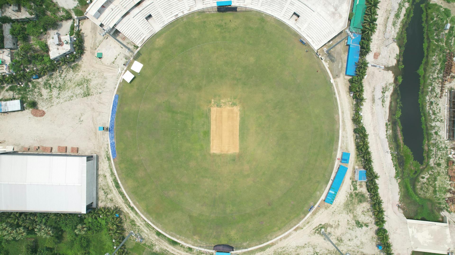 Top-down view of a cricket stadium in Dhaka, showcasing the pitch and surrounding areas.