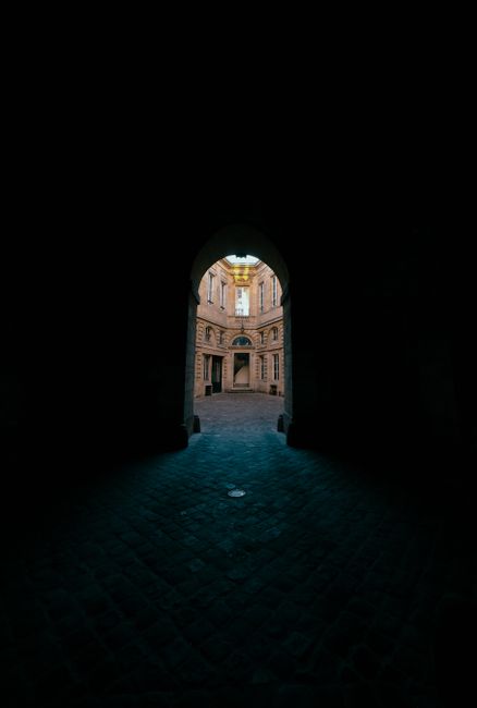 Explore a historic courtyard through a gothic archway, with dramatic lighting and shadows enhancing the architectural beauty.