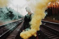 一名男子手持一枚充满活力的黄色烟雾弹，站在铁轨上，周围烟雾滚滚