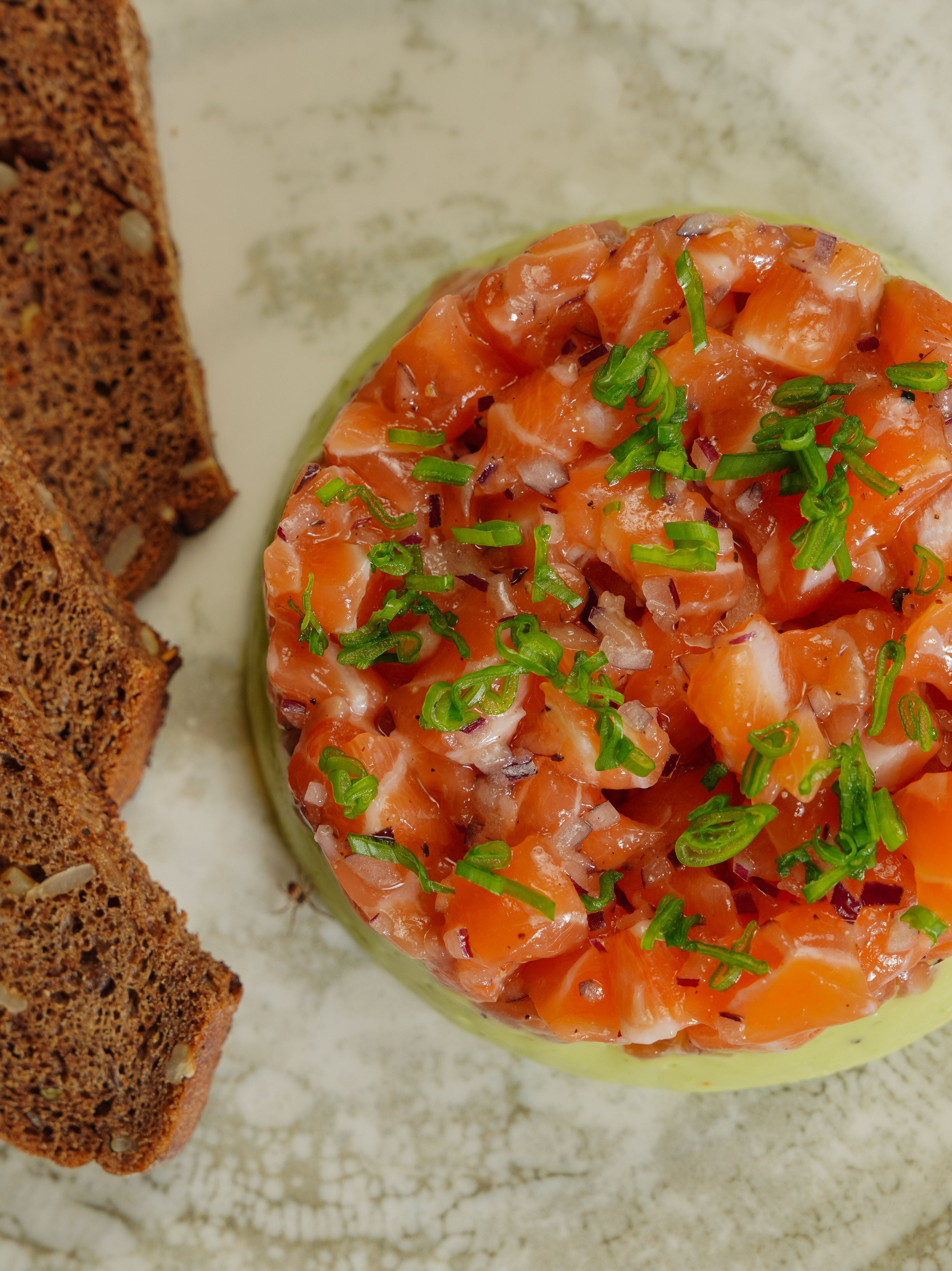 Delicious salmon tartare topped with herbs, served with rye bread slices. Perfect for gourmet appetizers.