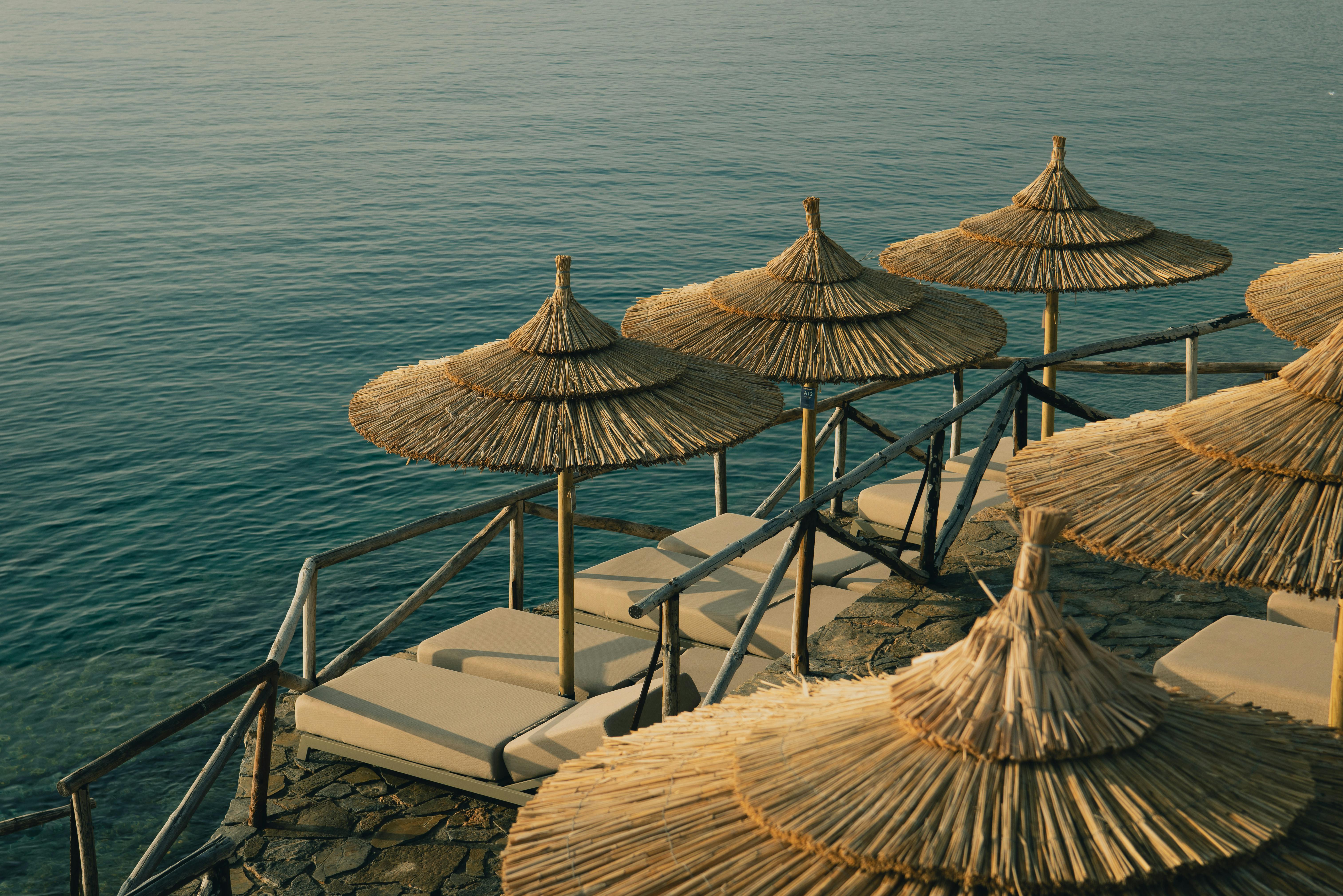 Relaxing beachside view with straw umbrellas and sunbeds by the sea, perfect for a summer getaway.