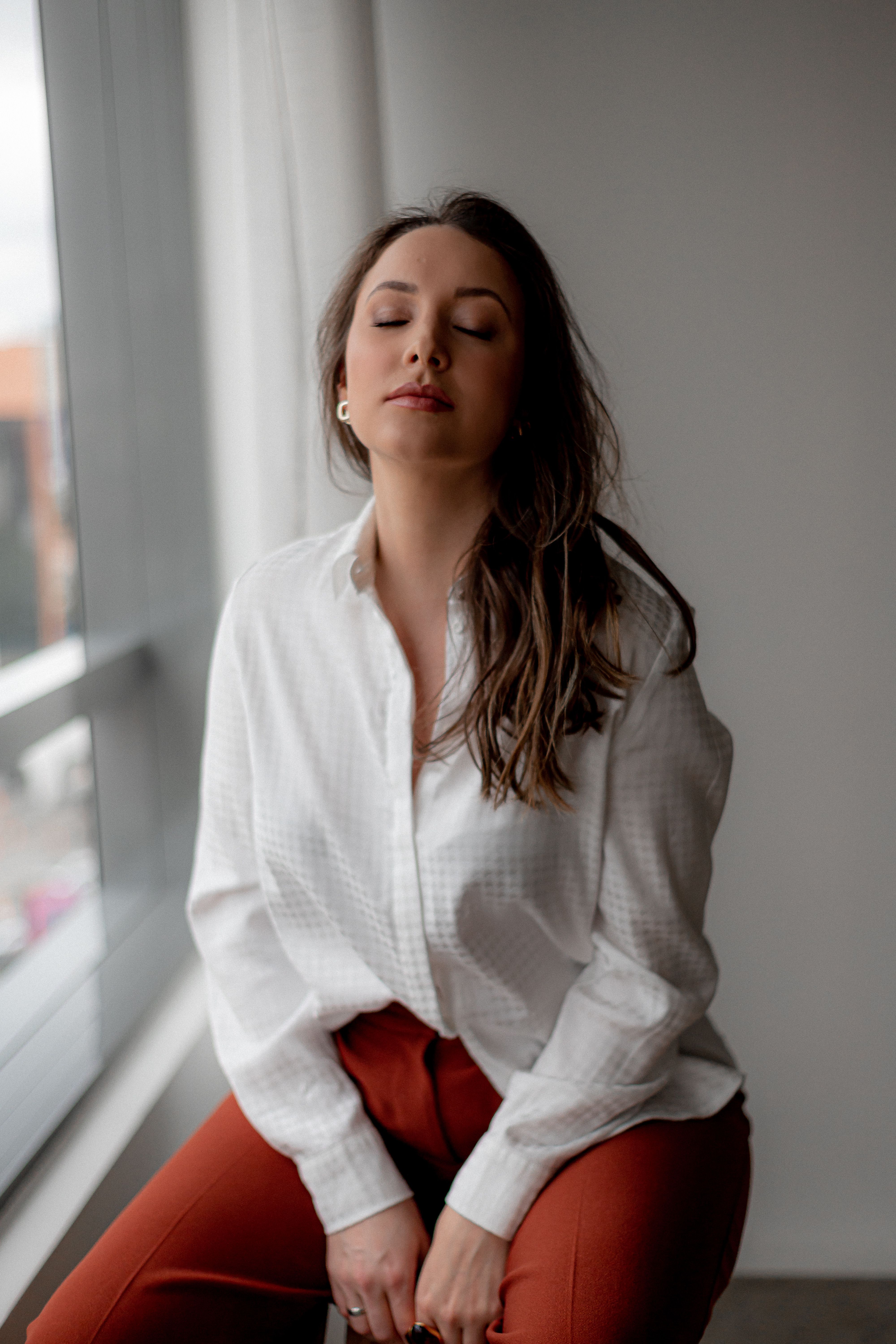 A Young Woman Sitting by the Window with Eyes Closed · Free Stock Photo